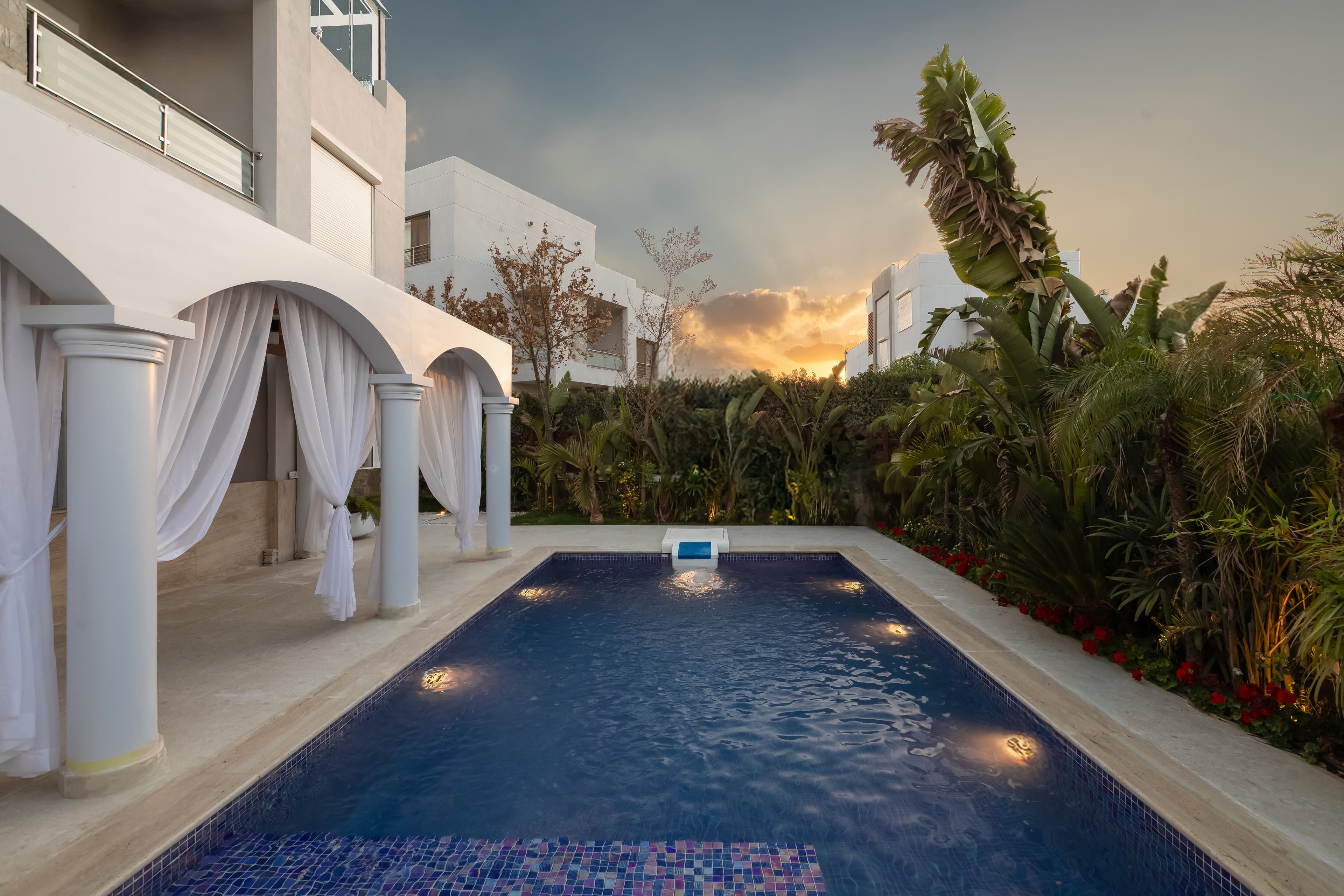 Luxury villa exterior with landscaped garden and pool at sunset